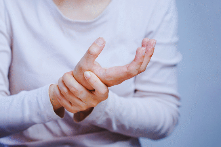 A person in a light long-sleeve shirt holds their left hand with their right, showing wrist pain—a common scene for um portador de LER e o direito à isenção do Imposto de Renda. The background is plain and light-colored.