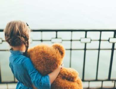 Back view of girl embracing a cute teddy bear looking to lake