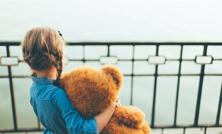 Back view of girl embracing a cute teddy bear looking to lake
