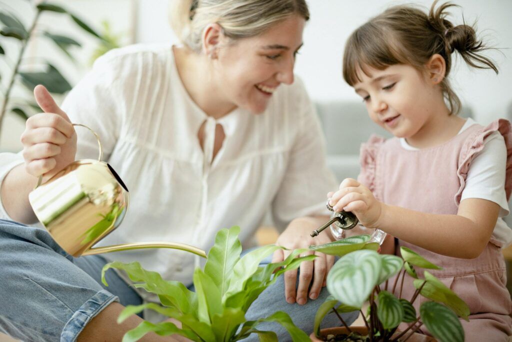 Kid watering potted plants with mom at home