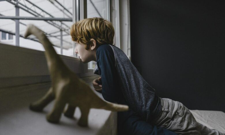 Sad boy leaning on window sill looking out of window in the evening